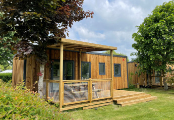 Prestige Cottage lodge in hout met terras, grasveld en omringd door bomen onder een bewolkte hemel.