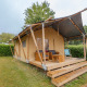 Safari-teltet Slow Lodge med træterrasse og havemøbler, omgivet af grønne hække og træer.