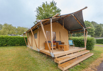 Tienda safari Slow Lodge con terraza de madera y muebles de exterior, rodeada de setos y árboles.