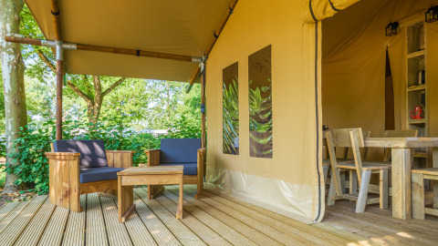 Zona exterior con sillones y mesa de madera en la terraza de una tienda safari rodeada de naturaleza.