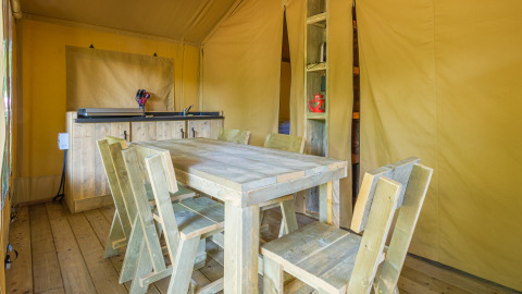 Zona de comedor de madera rústica dentro de una tienda safari en Slow Lodge, Camping Seasonova Haliotis, Francia.
