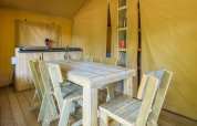 Eetgedeelte met houten meubels in een safaritent bij Slow Lodge, Camping Seasonova Haliotis, Frankrijk.