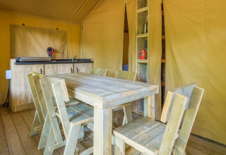 Zona de comedor de madera rústica dentro de una tienda safari en Slow Lodge, Camping Seasonova Haliotis, Francia.