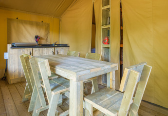 Rustic wooden dining area inside a safari tent at Slow Lodge, Camping Seasonova Haliotis, France.