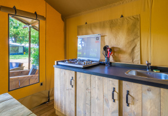 Interior of a safari tent featuring a wooden kitchen counter, gas stove, sink, and view to outdoor seating.