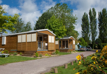Two charming wooden lodges with porches at Cottage Soleo, surrounded by greenery and blooming flowers.