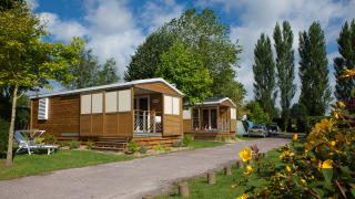 Two charming wooden lodges with porches at Cottage Soleo, surrounded by greenery and blooming flowers.