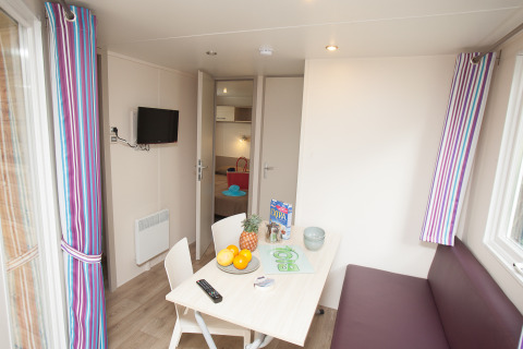 Vista interior del Cottage Soleo en Camping Seasonova Haliotis, Francia, con mesa de comedor y sofá.