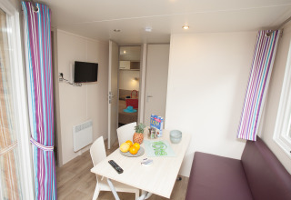 Innenansicht der Lodge Cottage Soleo im Camping Seasonova Haliotis in Frankreich mit Tisch und Sofa.