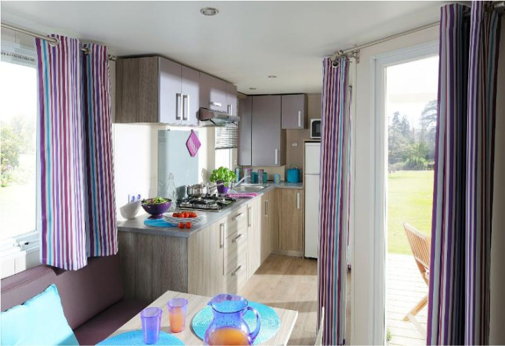 Modern kitchen and dining area in Cottage Soleo at Camping Seasonova Haliotis, with striped curtains.
