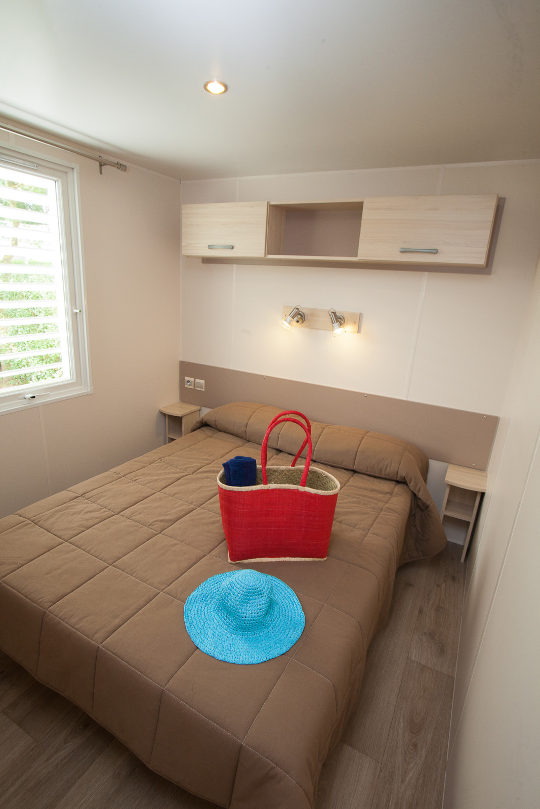 Slaapkamer in Cottage Soleo bij Camping Seasonova Haliotis in Frankrijk met bed, mand en blauwe hoed.
