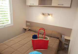 Dormitorio en Cottage Soleo en Camping Seasonova Haliotis en Francia con cama, bolsa y sombrero azul.