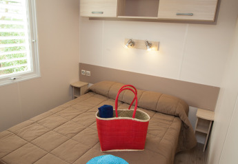 Slaapkamer in Cottage Soleo op Camping Seasonova Haliotis in Frankrijk met tweepersoonsbed, mand en hoed.