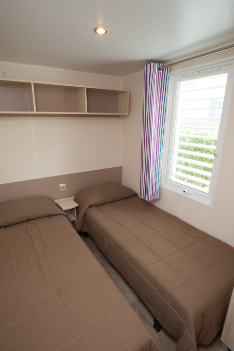 Habitación con dos camas individuales, ropa de cama marrón, estante de pared y cortina a rayas en Cottage Soleo.