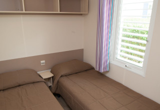 Habitación con dos camas individuales, ropa de cama marrón, estante de pared y cortina a rayas en Cottage Soleo.