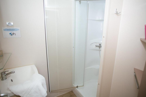 Pequeño baño con ducha y lavabo en Cottage Zen, Camping Seasonova Haliotis, Francia, paredes blancas.