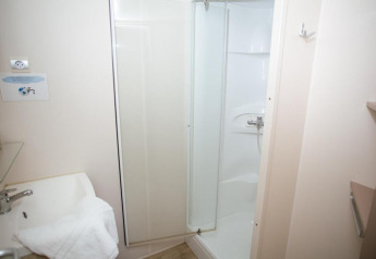 Pequeño baño con ducha y lavabo en Cottage Zen, Camping Seasonova Haliotis, Francia, paredes blancas.