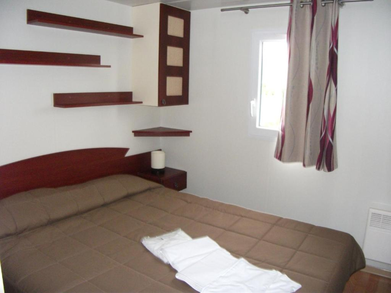 Slaapkamer met tweepersoonsbed, moderne planken, raam en gordijnen bij Cottage Zen, Camping Seasonova Haliotis.