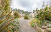 Pfad durch blühenden Garten zu Coco Sweet Safari-Zelten im Camping Seasonova Haliotis, Frankreich, bei bewölktem Himmel.