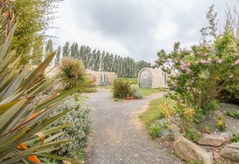 Camino entre jardines hacia tiendas Coco Sweet en Camping Seasonova Haliotis, Francia, bajo cielo nublado.