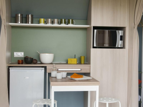 Pequeña cocina en una tienda safari en Camping Seasonova Haliotis, Francia, con microondas y mesa.
