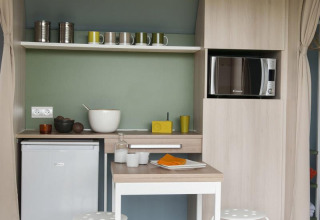 Pequeña cocina en una tienda safari en Camping Seasonova Haliotis, Francia, con microondas y mesa.