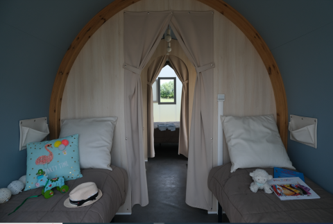 Vista interior de una tienda safari con dos camas individuales, cojines y juguetes en Camping Seasonova Haliotis, Francia.