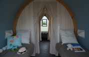 Vista interior de una tienda safari con dos camas individuales, cojines y juguetes en Camping Seasonova Haliotis, Francia.