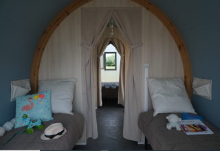 Vista interior de una tienda safari con dos camas individuales, cojines y juguetes en Camping Seasonova Haliotis, Francia.