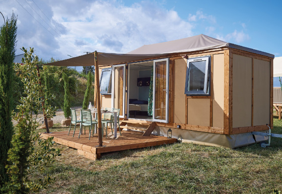 Vista exterior de la cabaña Corfou con terraza de madera, mesa, sillas y vegetación alrededor.