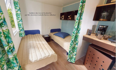 Vista interior de la cabaña Corfou con dos camas individuales, mesa de café y cortinas de hojas en Francia.
