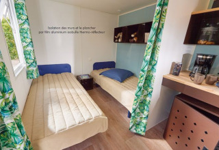 Vista interior de la cabaña Corfou con dos camas individuales, mesa de café y cortinas de hojas en Francia.