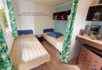 Intérieur du cabanon Corfou avec deux lits simples, un coin café et des rideaux verts aux Plages de Loire.