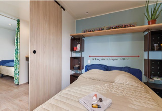 Dormitorio en la cabaña Corfou en Camping Seasonova Les Plages de Loire, con cama king size y estanterías.