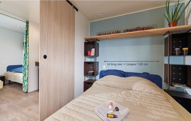 Dormitorio en la cabaña Corfou en Camping Seasonova Les Plages de Loire, con cama king size y estanterías.