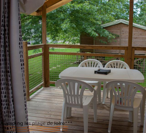 Wooden terrace with white plastic table and chairs at a glamping accommodation, facing green trees.