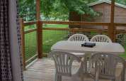 Terraza de madera con mesa y sillas de plástico blanco en glamping, rodeada de árboles y naturaleza.