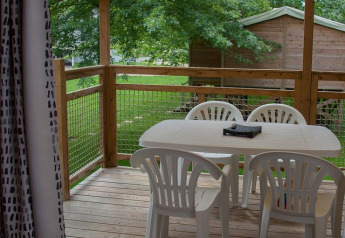 Terraza de madera con mesa y sillas de plástico blanco en glamping, rodeada de árboles y naturaleza.