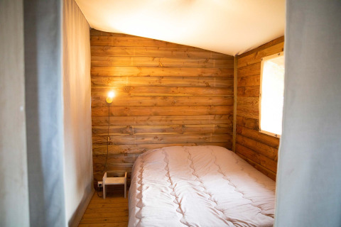 Cozy bedroom with wooden walls, double bed, and soft lighting in Eco lodge at Camping Seasonova Les Plages de Loire.