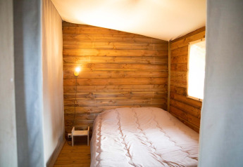 Petite chambre chaleureuse avec murs en bois et lit double dans l’Eco lodge au Camping Seasonova Les Plages de Loire.