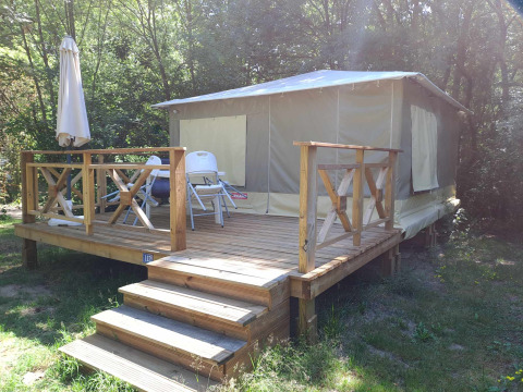 Cabina Bungalodge con terrazza in legno, sedie da giardino e ombrellone immersa nella natura.