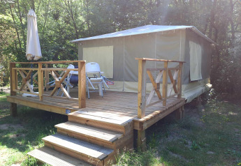 Bungalodge cabin with wooden deck, patio furniture, and umbrella, surrounded by a wooded area.