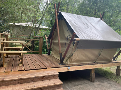 Bivouac tipi tent op verhoogd houten terras met zitbank, omgeven door groen en bomen in het bos.