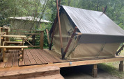 Bivouac telt på træterrasse med træbænk, omgivet af grøn skov, perfekt til glamping.