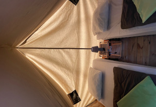 Binnenaanzicht van Bivouac tipi tent met twee bedden, kussens, dekens en lamp op houten vloer.