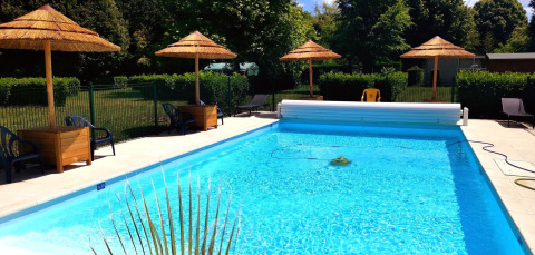 Heated swimming pool with thatched umbrellas at Camping Seasonova Le Martinet in Centre-Val de Loire, France.