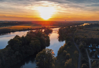 Solnedgang over floden ved Camping Seasonova Le Martinet i Centre-Val de Loire, Frankrig, med frodig natur.