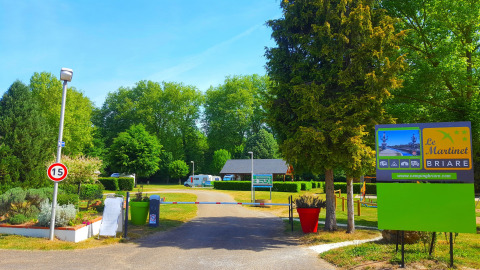 Ingresso di Camping Seasonova Le Martinet in Centre-Val de Loire, Francia, con alberi verdi e cartelli vistosi.