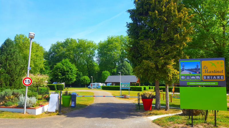 Entrée du Camping Seasonova Le Martinet en Centre-Val de Loire, France, entourée d’arbres avec panneaux colorés.