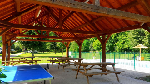 Covered wooden pavilion with picnic tables and ping pong table at Camping Seasonova Le Martinet in France.